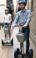 young couple guy and girl walking on segway in streets of european city