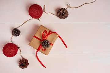 Christmas composition. Red shiny balls, gift box with red ribbon, pine cones on a light wooden background.