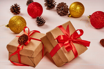 Christmas composition. Gold and red shiny balls, gift box with red ribbon, pine cones on a light wooden background.