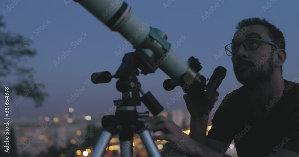 Wall mural astronomer with a telescope watching at the stars and moon with blurred city lights in the backgroun
