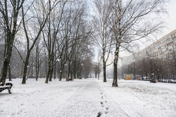 The first snow falls on a Park bench. Snow storm, snowstorm in the city. The first snow on a dark path and footprints on it. Heavy snowfall in the Park, large snowflakes fall on the sidewalk.
