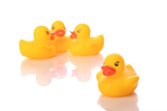 Bullying, hermit concept. One mini yellow rubber duck stands alone while group of ducklings talks about him isolated on white background. Dislike, enmity, distaste, loneliness, gossip. Copy space