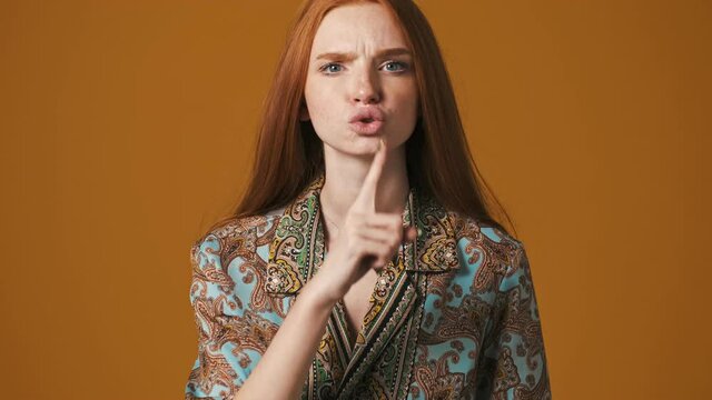 A displeased young woman is doing silence gesture standing isolated over brown background