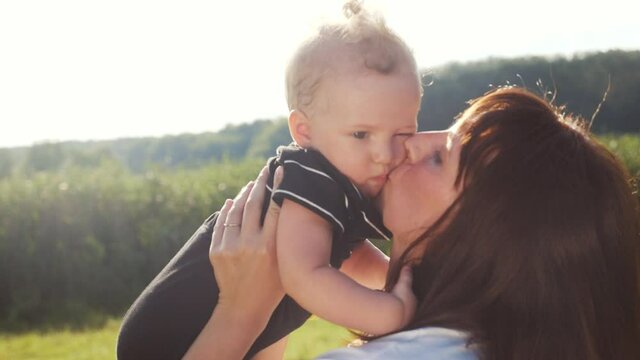 mom kiss newborn baby son holds in his arms playing in the park. mother day kid dream childhood happy family concept. parent play on hands with a little boy son lifestyle sunlight. people in the park