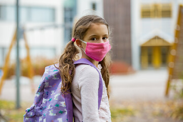 Schoolgirl wearing protective fabric reusable face mask going to school. School education during the coronavirus pandemic. Security measures and social distancing