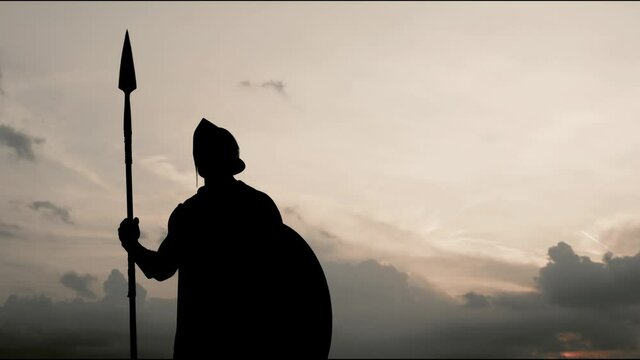 Silhouette of man in armour posing with spear in field.