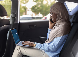 Black muslim businesswoman using laptop and cellphone in car, going to work