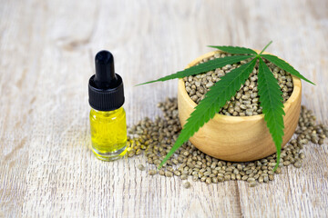 Cannabis seeds in a wooden cup, cannabis leaves are placed on top. And hemp oil extracted in a glass bottle Disease treatment ideas using hemp oil Alternative medicine Empty space to place text.