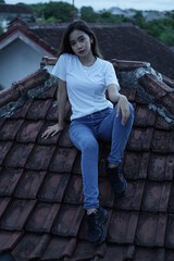 The blonde girl is sitting and stylish wearing a white T-shirt on the roof of the house with a view of the clear sky. female t-shirt models for mockups and templates.