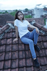 The blonde girl is sitting and stylish wearing a white T-shirt on the roof of the house with a view of the clear sky. female t-shirt models for mockups and templates.