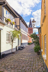 Cobbled street at the old town of Aalborg, Denmark, with bell tower of  Vor Frue Kirke in background