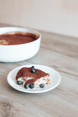 Delicious tiramisu slice of cake on white plate with blueberry berries, vertical orientation photo