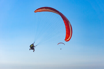 Paragliding in the sky. Paraglider tandem flying over the sea with mountains at sunset. Aerial view...