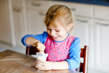 Little toddler girl eating yogurt for breakfast. Cute healthy baby sitting in the kitchen or at...
