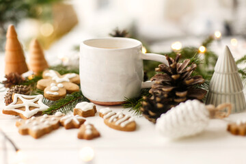 Coffee, homemade gingerbread cookies, pine cones decorations and warm lights on white  table