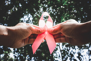 Woman's hand holds a pink ribbon with a ray of hope. Symbolic display on World Breast Cancer Day in...
