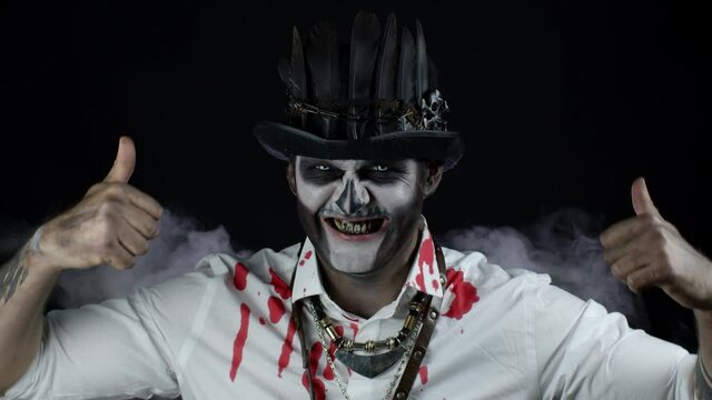 Frightening smiling man in skeleton Halloween costume showing thumbs up gesture. Black background