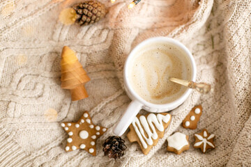 Warm coffee on background of cozy knitted sweater, christmas gingerbread cookies, lights
