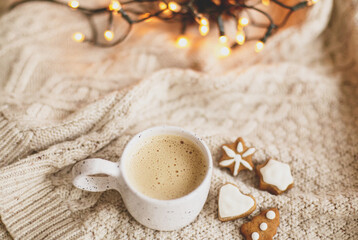 Warm coffee in stylish cup on cozy knitted sweater with christmas gingerbread cookies and lights