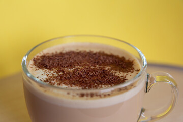 mug of coffee with milk sprinkled with chocolate chips, and foam, on yellow background. Energy and cheerfulness in morning.