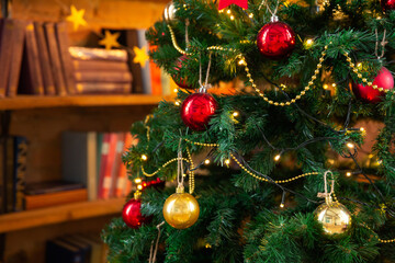 Fototapeta premium Christmas tree decorated with garlands and balls, against background of library bookshelves. New Year or Christmas background. Greeting card.