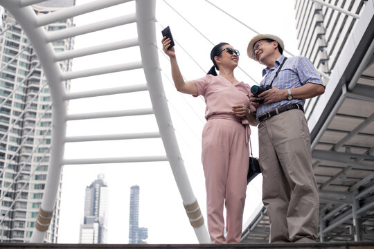 Senior Asian couple selfie by mobile outdoors.