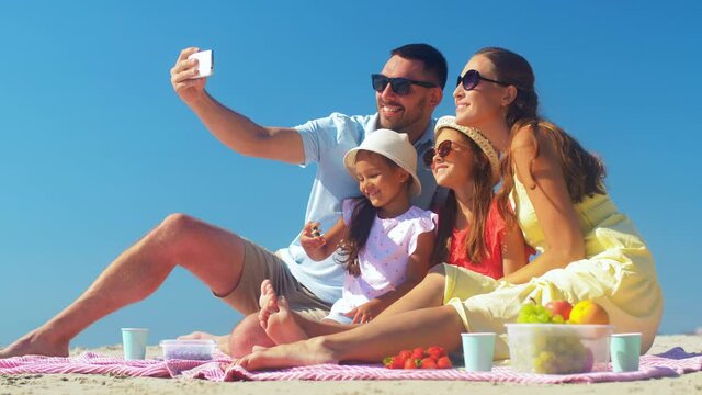 family, leisure and people concept - father, mother and two little daughters taking selfie on summer beach