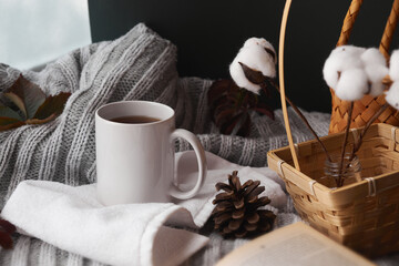 Cozy home decor with a warm atmosphere. White mug with hot tea and knitted clothes