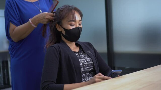 Asian hairdresser woman wearing medical face mask cutting hair of woman customer at office . new normal during  Coronavirus pandemic or Covid-19 outbreak