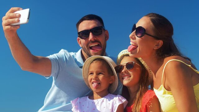 family, leisure and people concept - father, mother and two little daughters taking selfie on summer beach