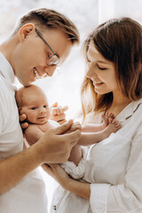 Happy young parents with newborn baby girl, loving mom hold little daughter in arms, caring dad gently hold a hand of adorable baby girl, tender family moments, parenting concept