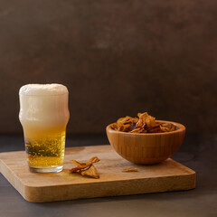 Cold beer in a glass a and bowl of vegetables chips crisps on a wooden try.