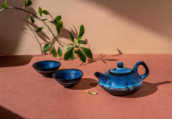 Blue teapot and tea cups, flowers branch on brown background. Copy space. Traditional asian tea ceremony concept.