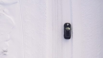 Aerial top view from drone of suv vehicle driving on snowy ice road exploring local landscapes in winter, bird&rsquo;s eye view of automobile car moving on area in snow