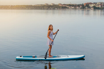 Young woman floats on the water of the lake on a sap board with an oar