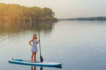 Fototapeta na wymiar Young woman floats on the water of the lake on a sap board with an oar