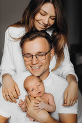 Overjoyed parents with newborn baby girl, loving dad gently hold little daughter in arms, beautiful mother hug caring father, smiling, enjoy happy moments, young family concept