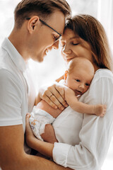 Beautiful parents with newborn baby girl, loving mom hold little daughter in arms, caring husband gently hug adorable wife, smiling, enjoy tender family moments, parenting concept