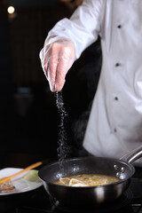 The process of making risotto. The chef adds salt to the seafood risotto. Unrecognizable vertical photo without a face.