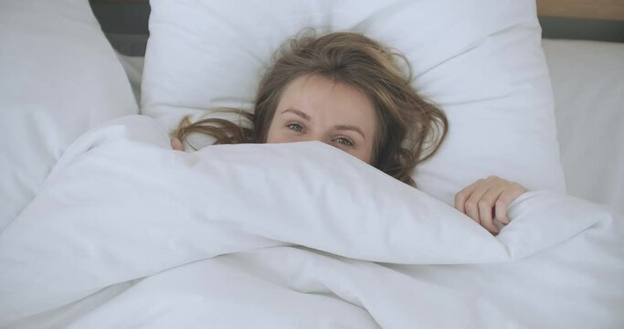 Happy Woman peeking out from her blanket in bed and Smiling. Peeking under duvet and smiling