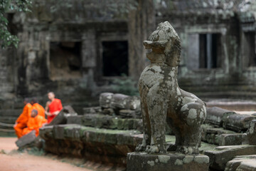Fototapeta na wymiar Focus on the great lion sculpture and blurred focus on the monks on the background at Ta Prohm temple, Siem Reap, Cambodia.