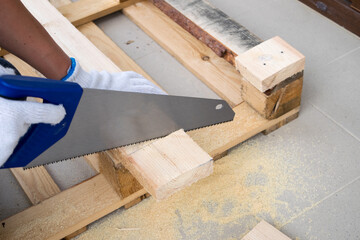 A man in white construction gloves is cutting a wooden plank - obrazy, fototapety, plakaty