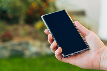 close-up shot of male hands holding smartphone with blank screen copy space for your text message or information content, against green nature background