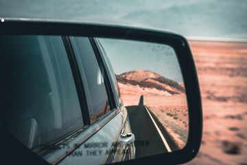 View through the side mirror to the back where a long road leading into nothing in the death valley is visible