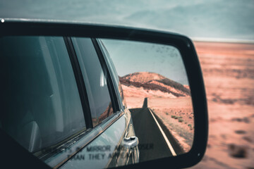 Naklejka premium View through the side mirror to the back where a long road leading into nothing in the death valley is visible