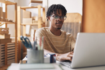 African young man in eyeglasses sitting at the table and working online on laptop at office