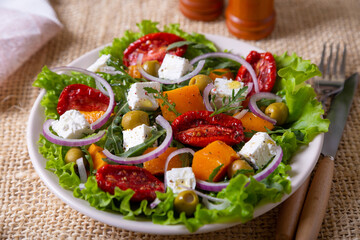 Warm salad with pumpkin, feta cheese, sun-dried tomatoes, olives, arugula and red onion. Close-up.