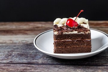 Chocolate cake with red cherries  Placed in a plate on an old wooden floor against a black background.