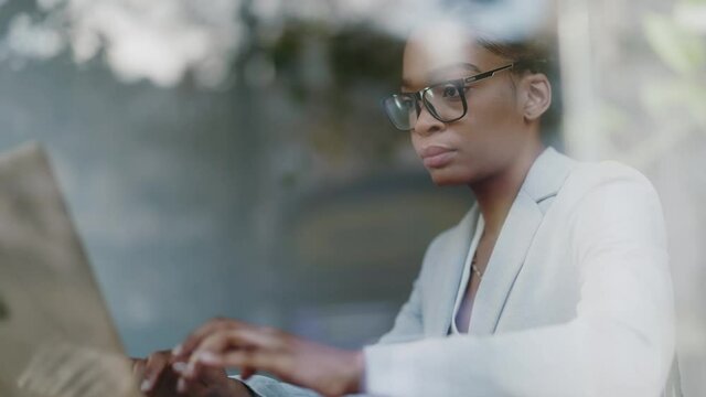 Confident young african american businesswoman typing keyboard of laptop computer working distantly online in the cafe. Through a window. Business people. Career concept.