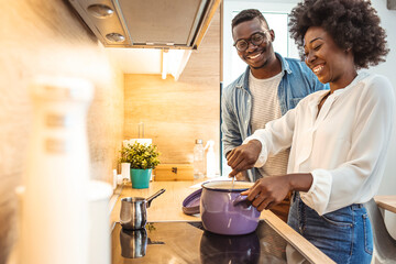 Beautiful young couple is talking and smiling while cooking healthy food in kitchen at home. Romantic couple is cooking on kitchen. Handsome man and attractive young woman are having fun together